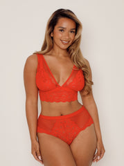 Woman wearing a red lace lingerie set against a plain background